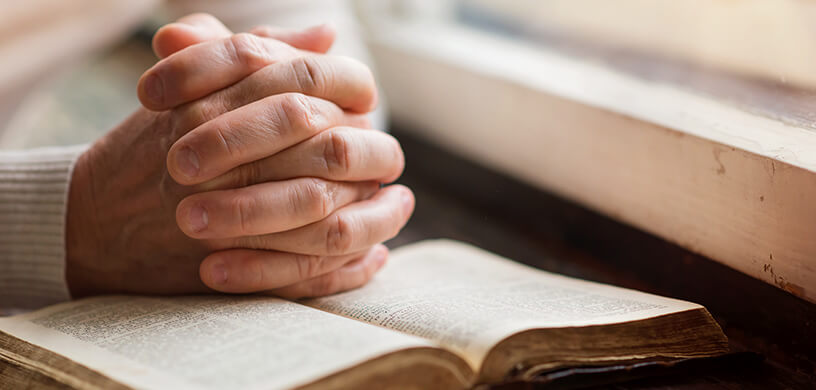 man-holding-hands-in-prayer-over-book